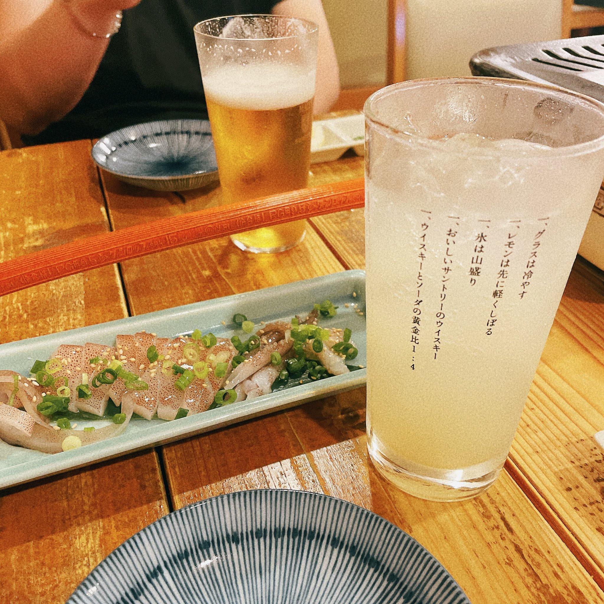 お通しのイカとレモンサワー。奥には鉄板が見える。