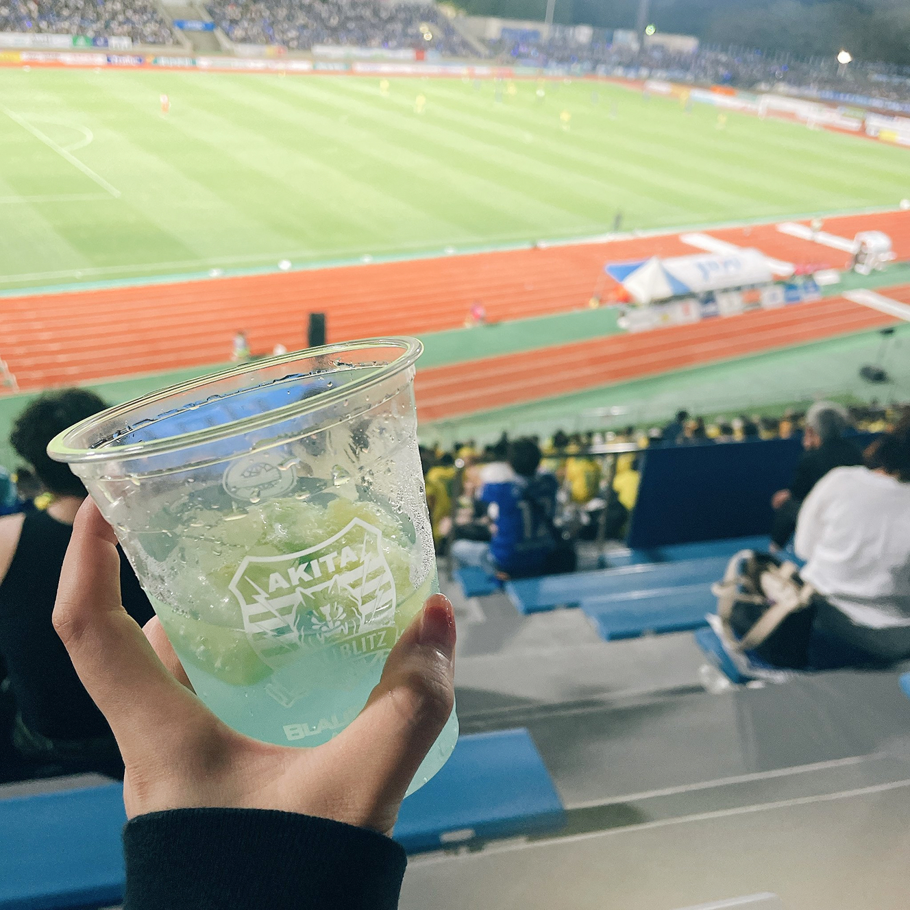 背景にはサッカースタジアムが広がっている。手前にはレモンサワーが写っている。