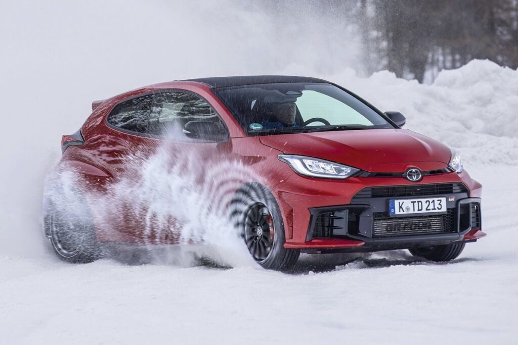 赤い車が雪原を雪煙をたてながらドリフトとする様子