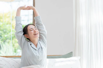 朝ベッドで起床し伸びをする女性