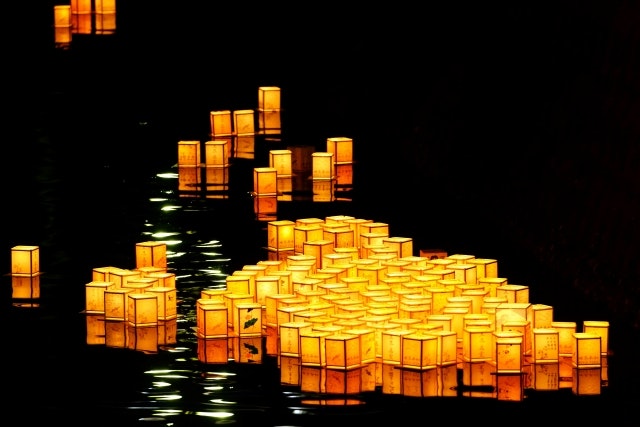 Lit paper lanterns floating down a river at night.