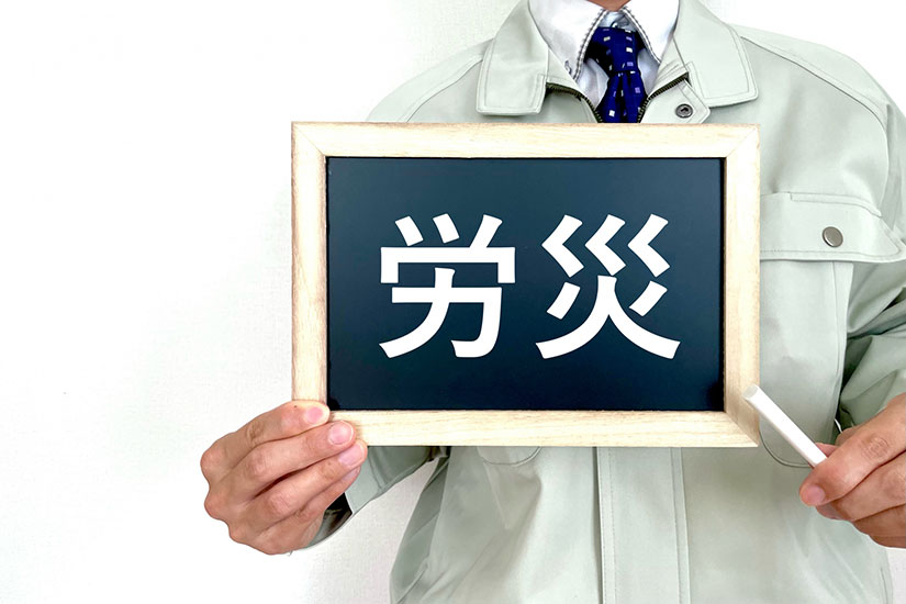 作業着の男性が黒板に書かれた労災の文字を示している