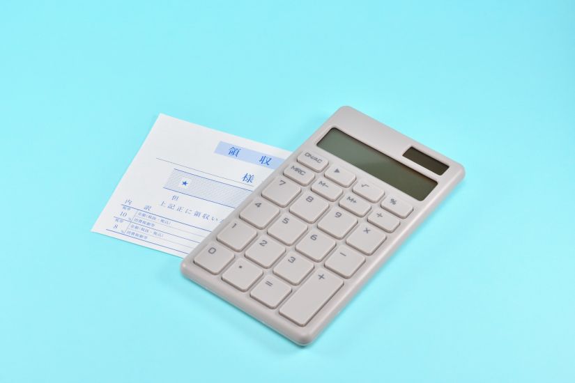 レシートと電卓が水色の背景に置かれており、経費計算や会計作業を表している。
