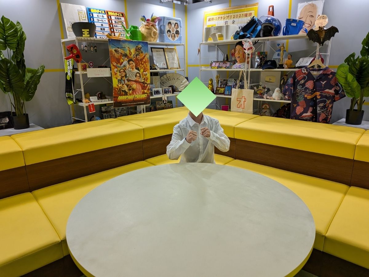 オモコロチャンネルのスタジオ再現コーナーの黄色いソファ中央でファイティングポーズを取る筆者。