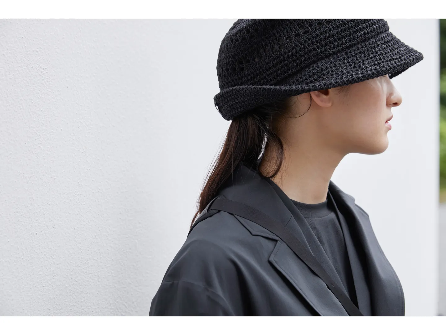 The same woman as in the previous photo, shot from the side, showing the shoulders up. She wears a hat with the brim folded up only at the back.