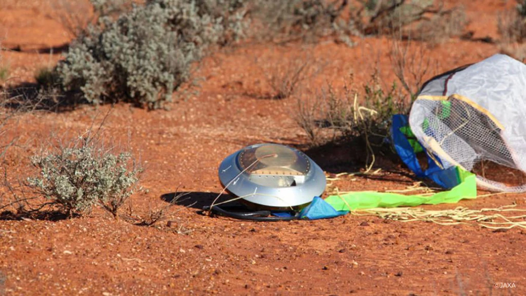 Photo of Hayabusa's re-entry capsule. The open parachute can be seen on the red soil.