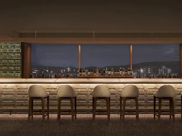 A bar counter with stools facing a window onto the night-time city