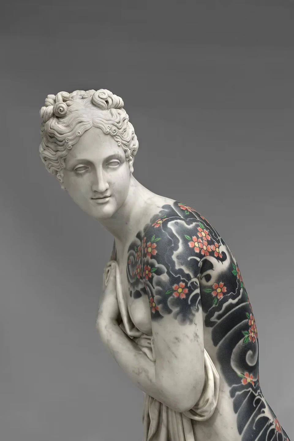 A female figure glancing back against a grey background, black waves and cherry blossoms flowing over her shoulder and back