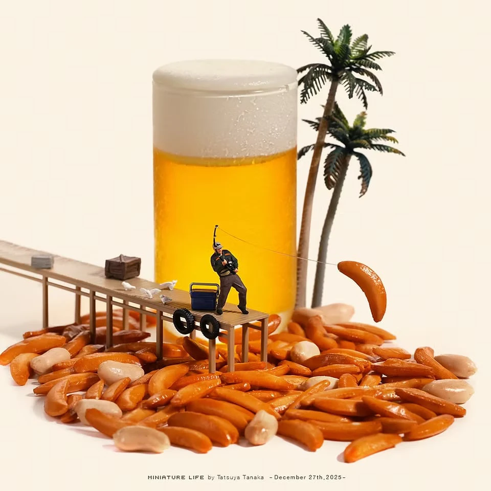 A glass of beer behind a shore made of kaki no tane rice crackers and peanuts; on a jetty, a fisherman reels in a cracker beside two palm trees
