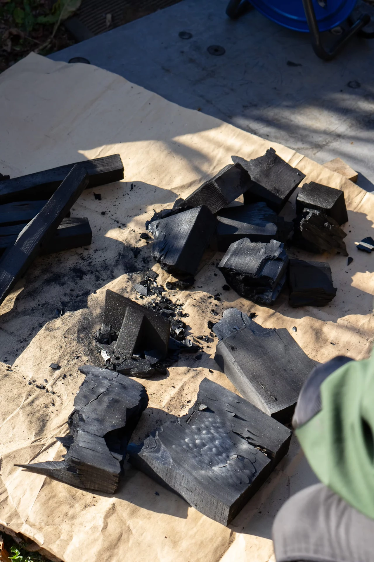 Freshly carbonised pieces of hinoki piled on paper in an outdoor workspace