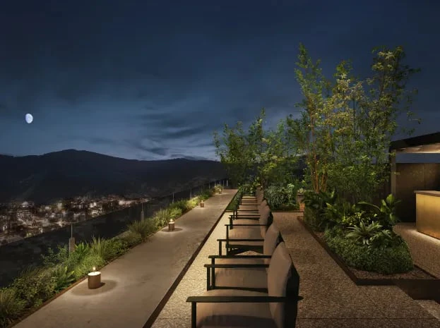 A rooftop terrace at night, with loungers among the planting and the Higashiyama hills and moon beyond