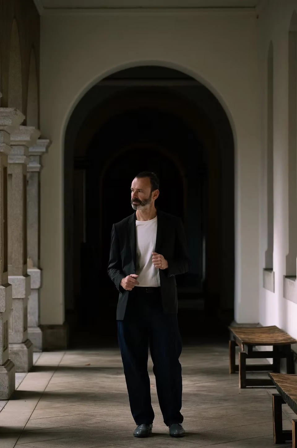 A man holding the lapel of his jacket before a dark archway