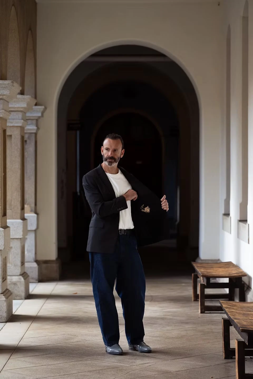 A man in a stone arcade holding open his black jacket to reveal the motif on its lining