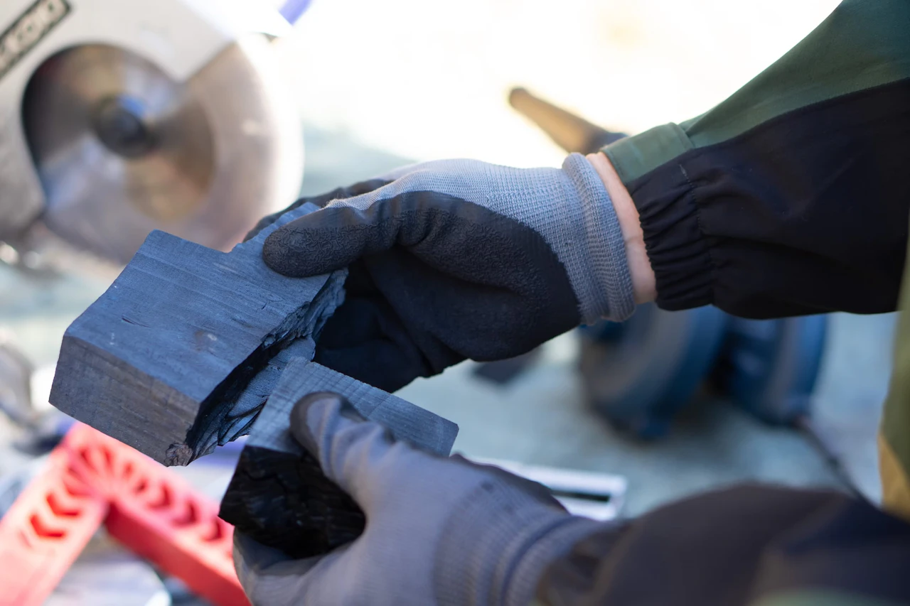 Gloved hands holding a carbonised block against a cutting saw