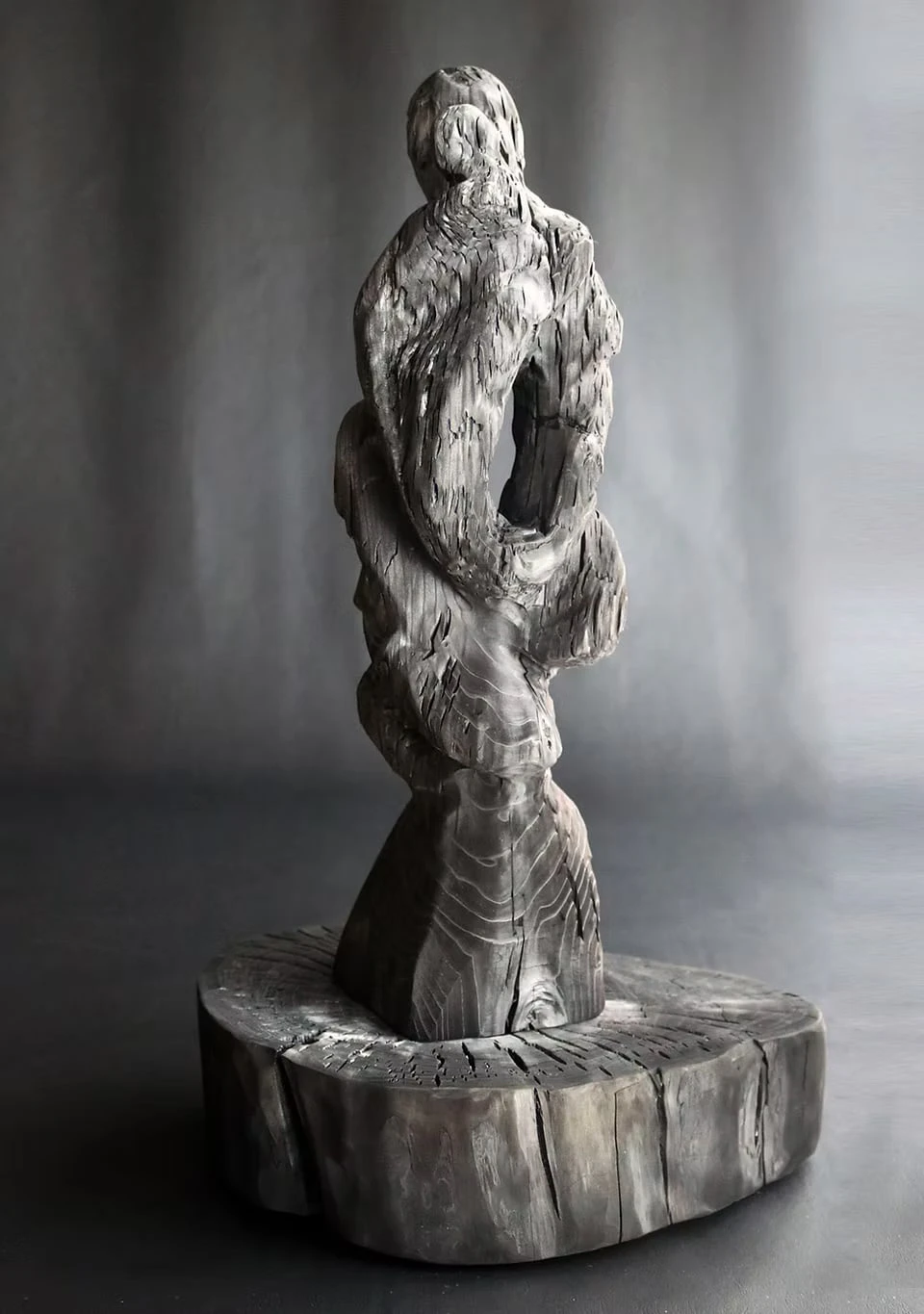 A figure-like charcoal sculpture standing on a base cut from a tree trunk