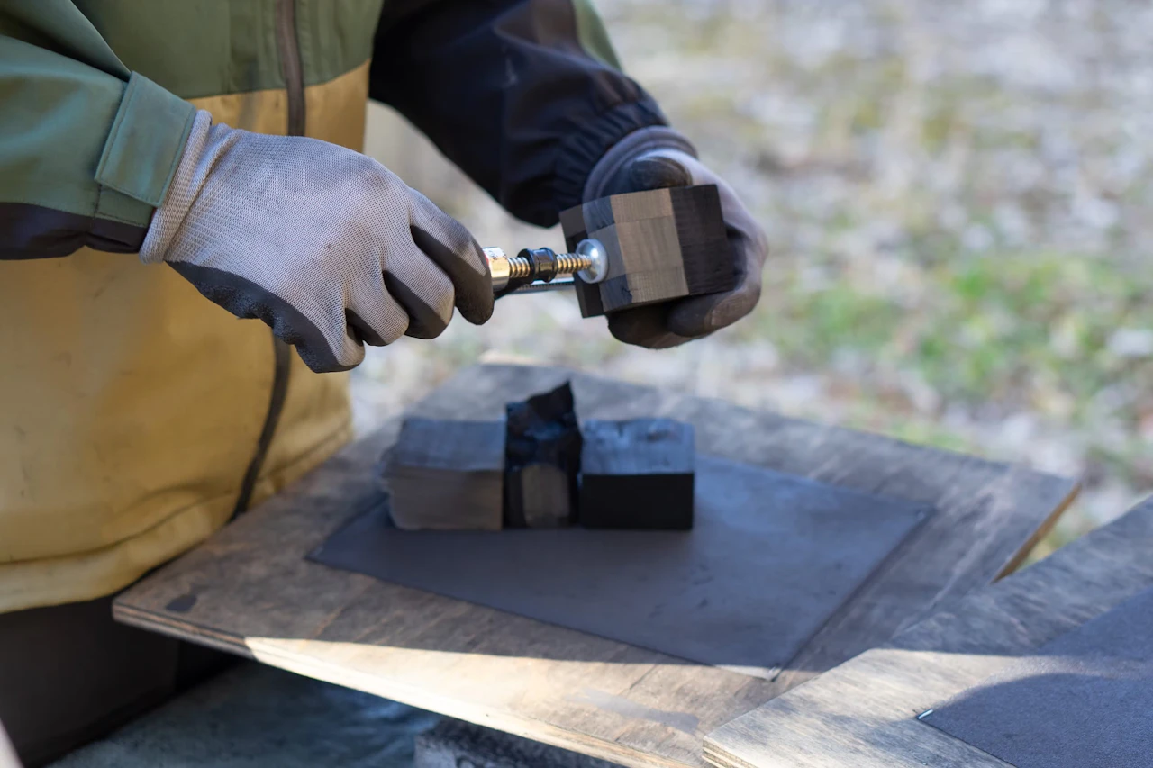 A gloved hand shaping a small piece of charcoal with a rotary tool