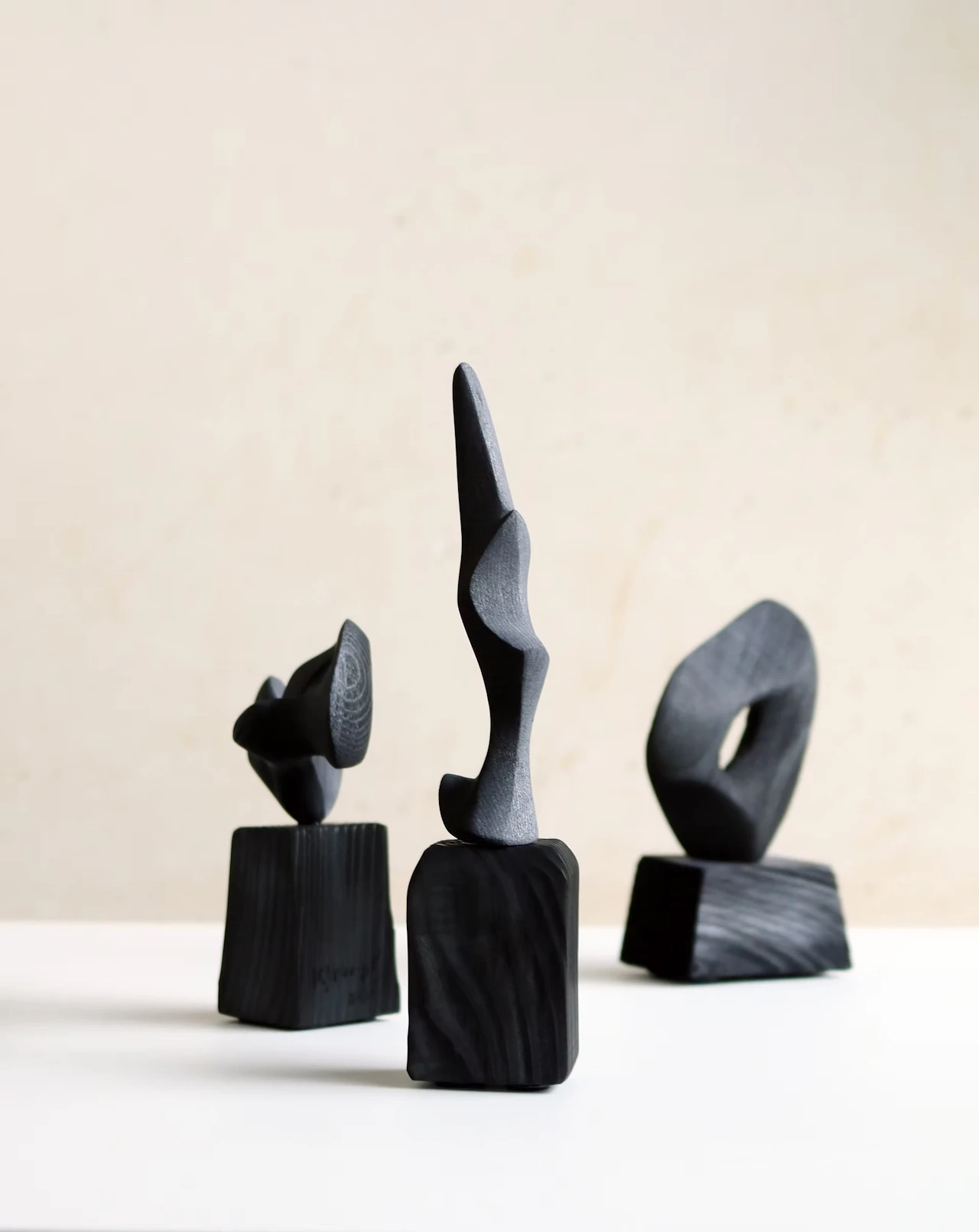 Three small, curving charcoal sculptures on black block bases