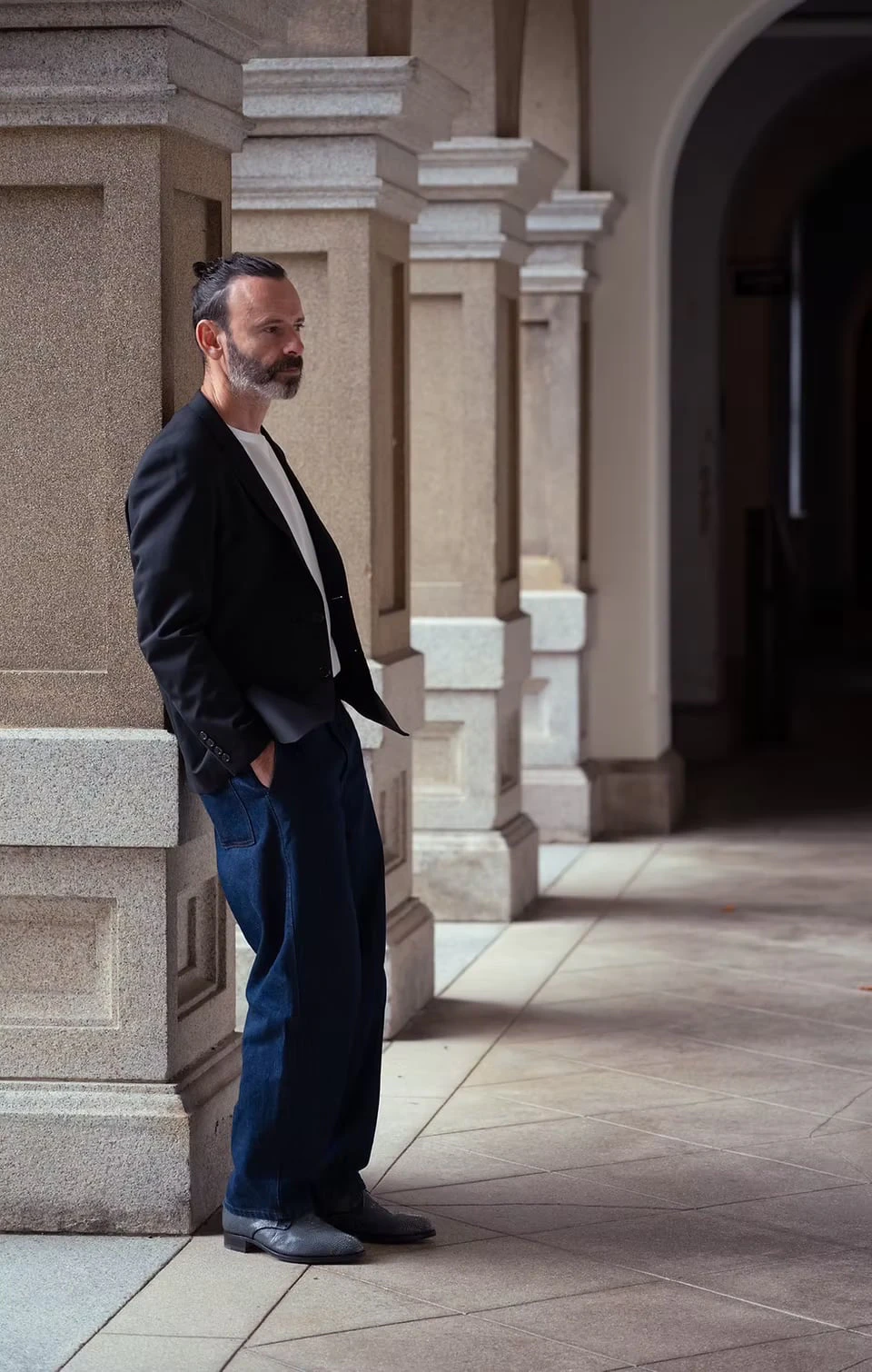 A man leaning against a stone pillar of an arcade, hands in his pockets