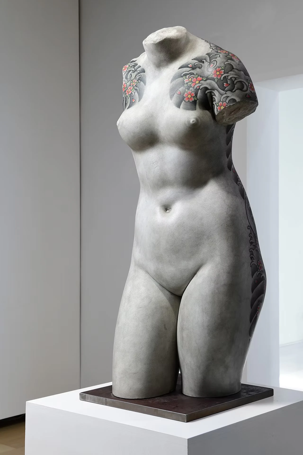 A female torso in a white gallery, waves and cherry blossoms tattooed on both shoulders and down one side