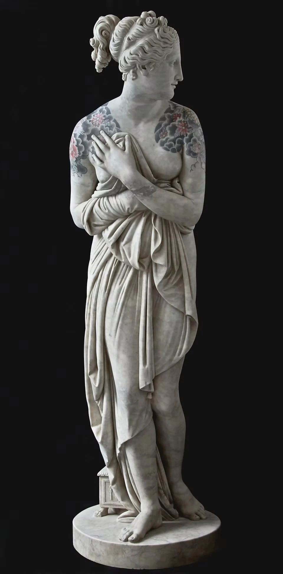 A marble female figure against a black background, holding a cloth to her chest, cherry blossoms and clouds tattooed on both shoulders
