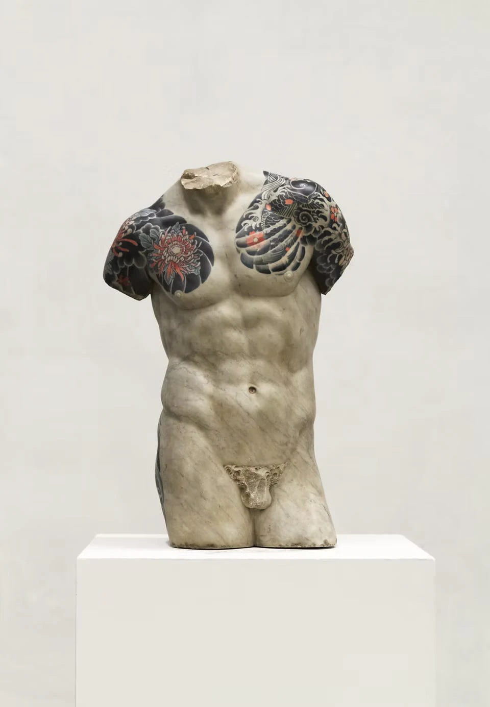 A male torso on a white plinth, chrysanthemums, waves and a feather-like motif tattooed across the shoulders and chest