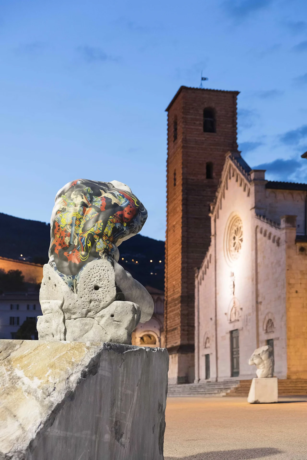 A torso with a vividly tattooed back on a stone block in front of a church at dusk