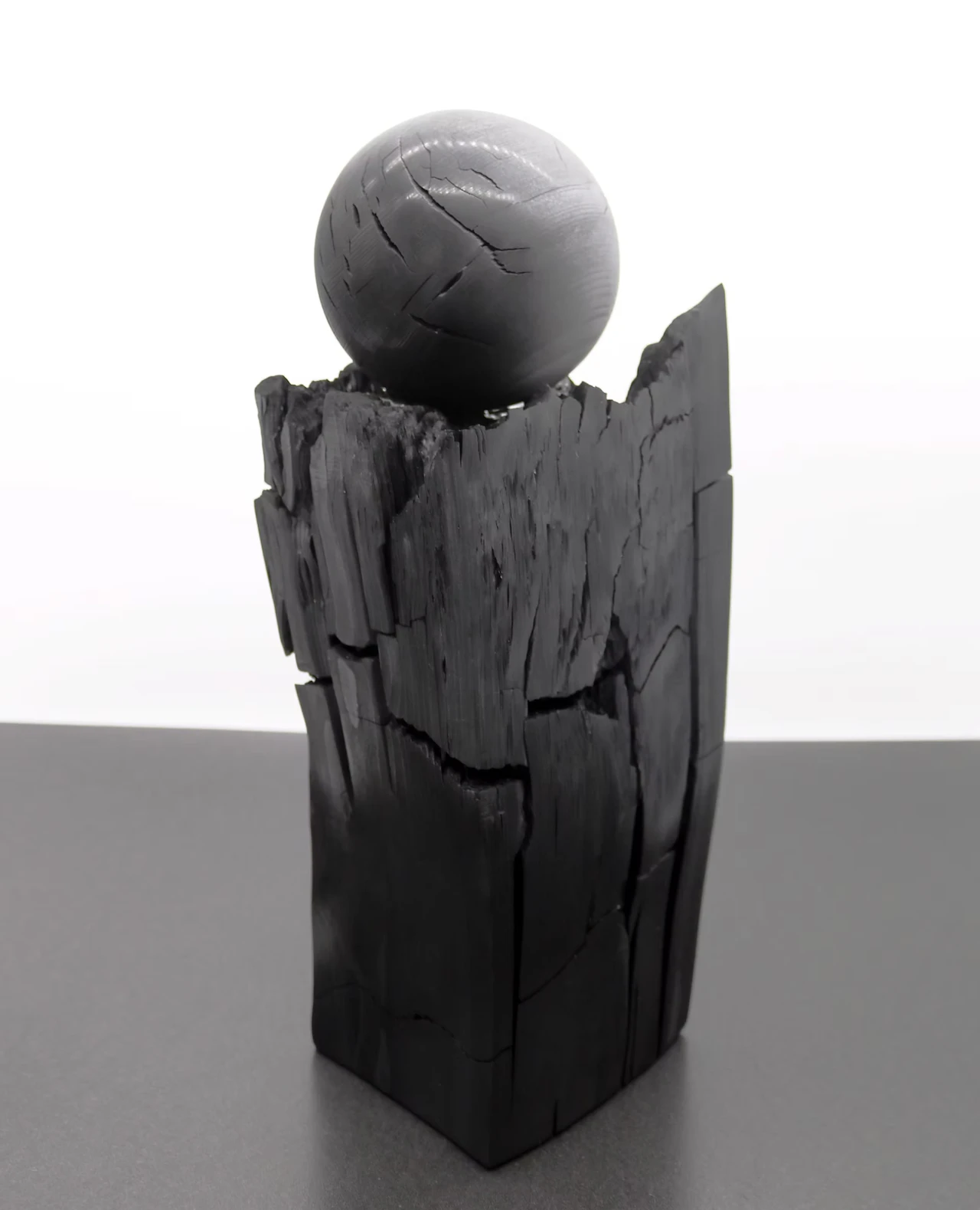 A carved sphere on top of a split charcoal column, against a white background