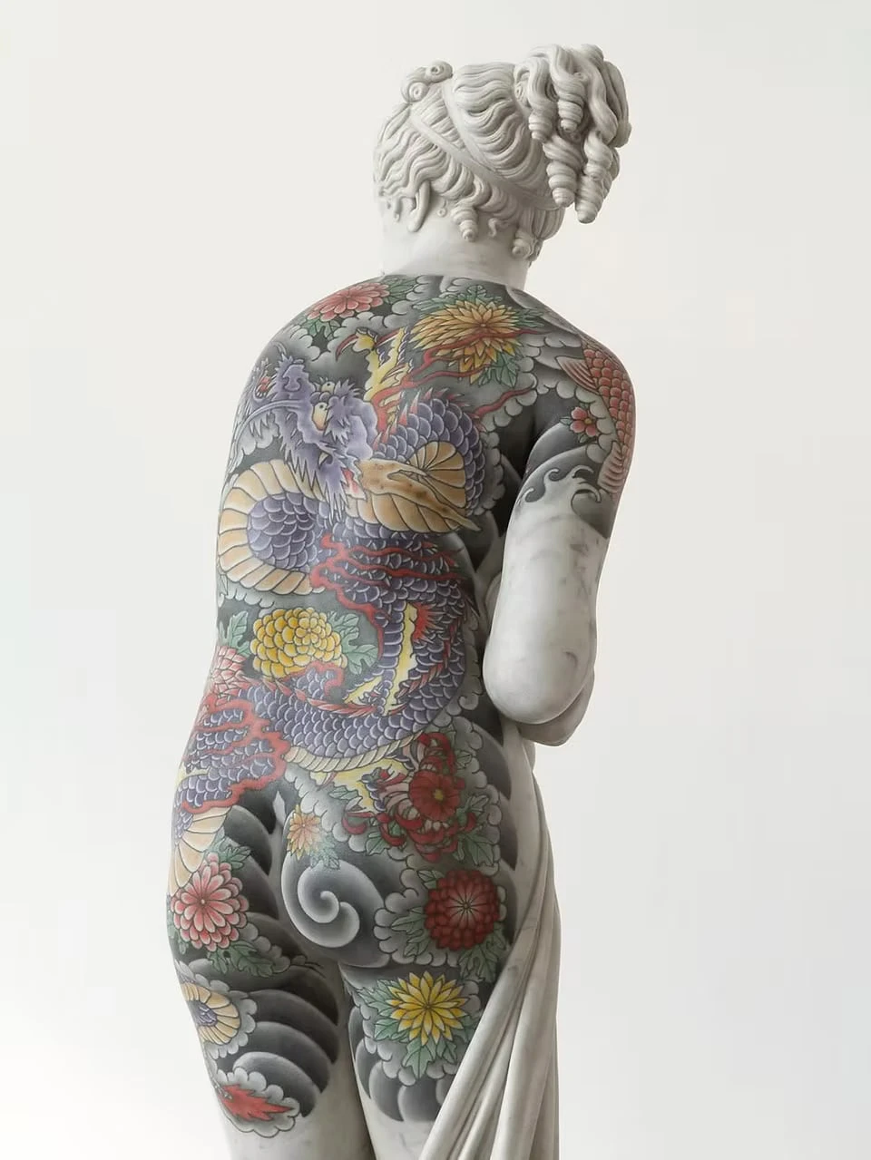 Close-up of a marble female figure's back, a purple dragon among yellow and red chrysanthemums and grey waves carved into the white stone