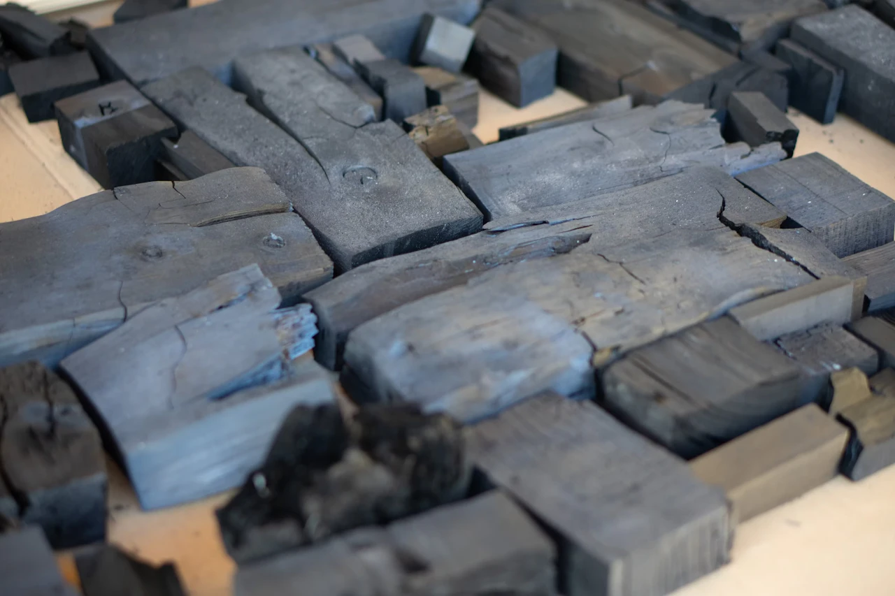 Blocks of carbonised hinoki laid out on a worktable, their surfaces gleaming a bluish black