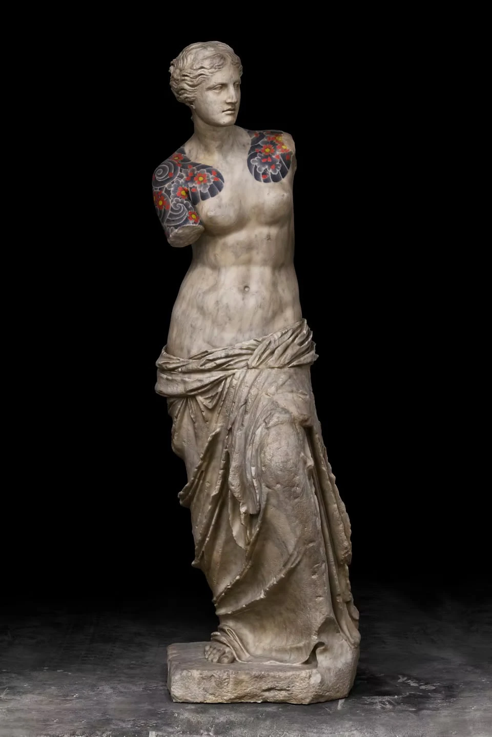 An armless female figure against a black background, waves and red flowers tattooed on both shoulders