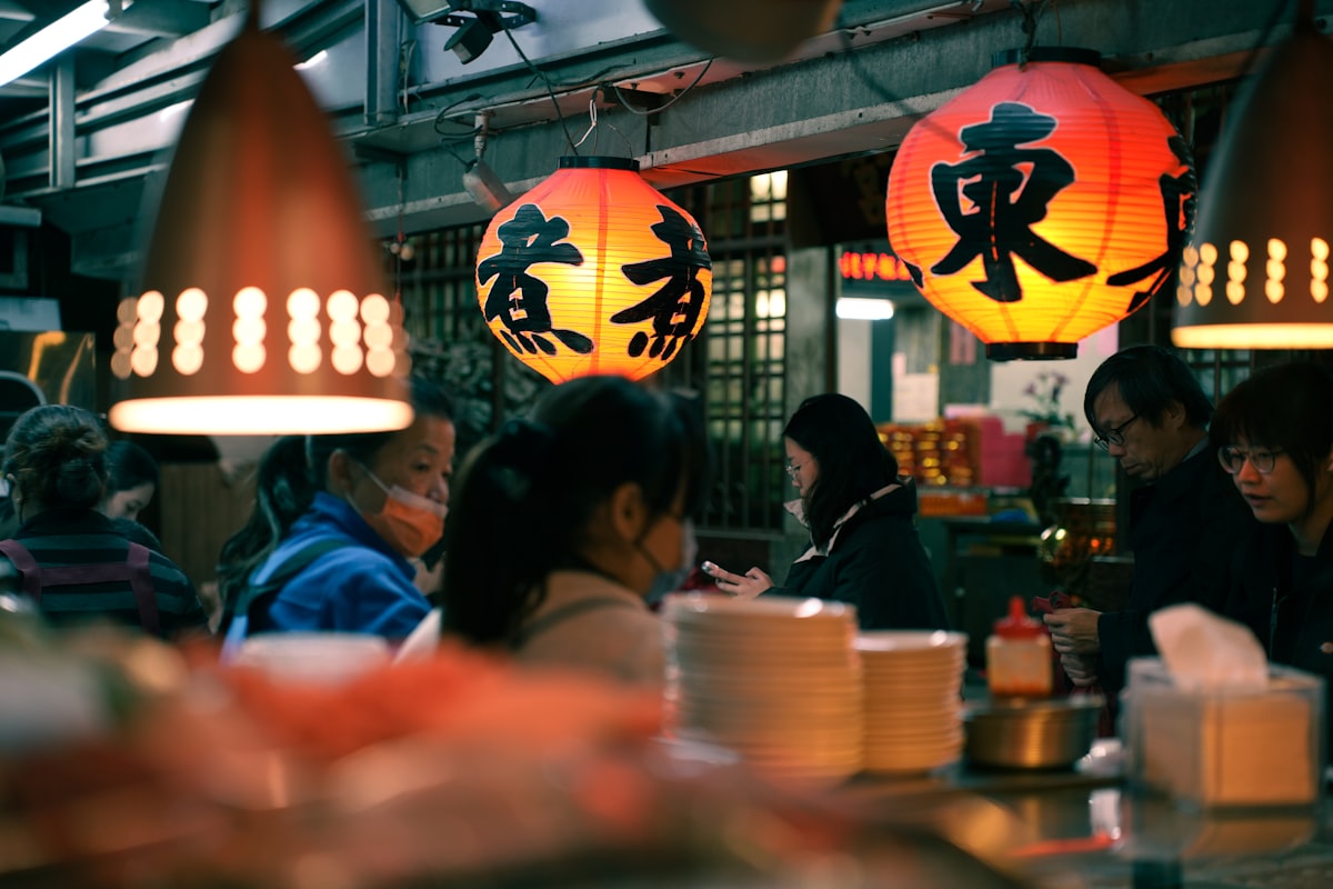 People sit at a restaurant with glowing lanterns overhead.