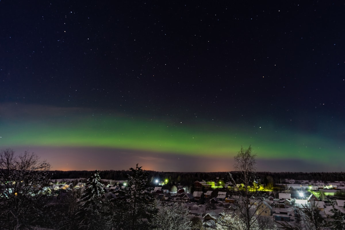 a green and purple aurora over a city at night