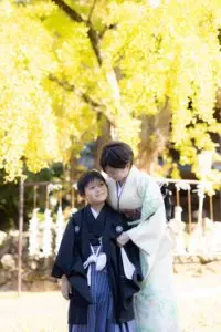 満開の銀杏の木の下でお母様が息子さんに優しく寄り添う七五三の親子ショット