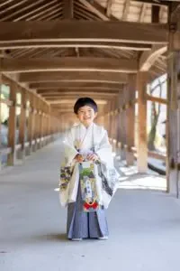 岡山県の吉備津神社にある美しい回廊で、白と水色の羽織袴を着た男の子が笑顔で佇む七五三の記念写真