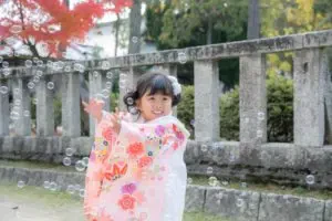 岡山県の吉備津彦神社の境内で、色とりどりのしゃぼん玉に両手を伸ばして笑う七五三の女の子