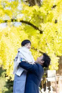 銀杏が色づく吉備津神社で、お父様がお子様を抱き上げて笑い合う七五三の一コマ