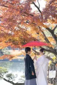 後楽園の紅葉と赤い和傘を手にした白無垢姿の新婦様、新郎様と寄り添うシーン