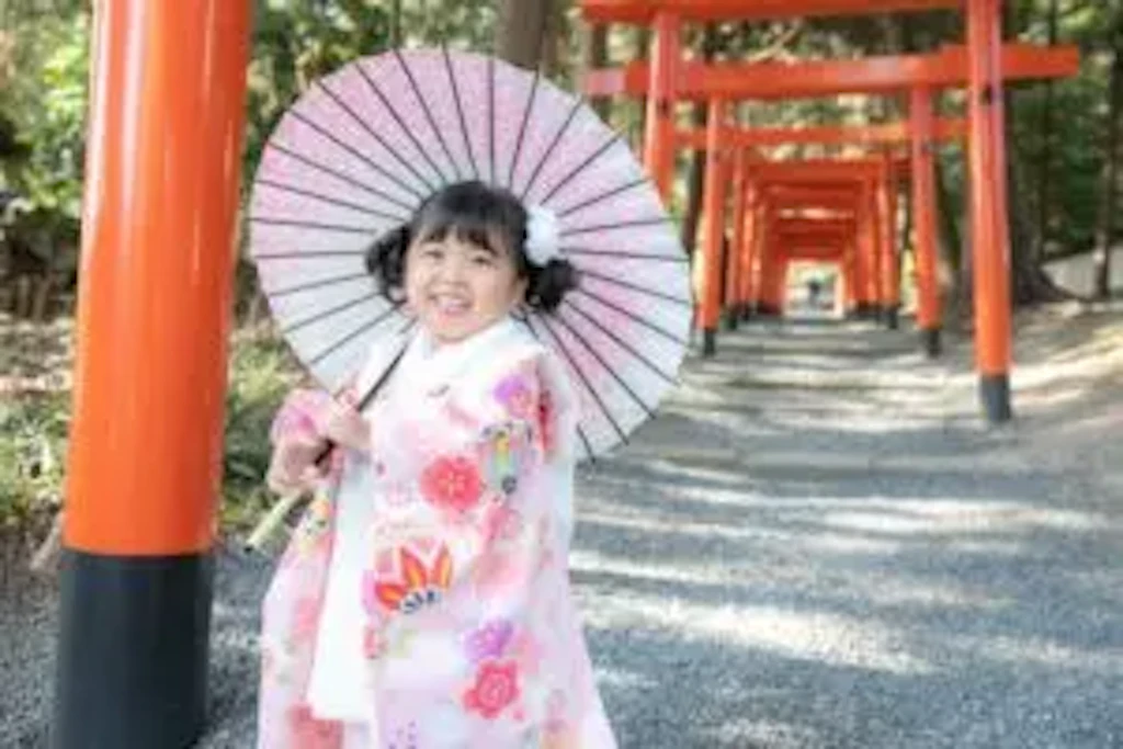 吉備津彦神社の朱色の鳥居が連なる参道で、和傘を差してポーズをとる七五三の女の子