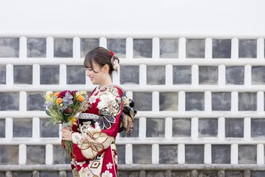 白い壁の前で花束を持ち振袖姿の女性が微笑んでいる横顔の写真