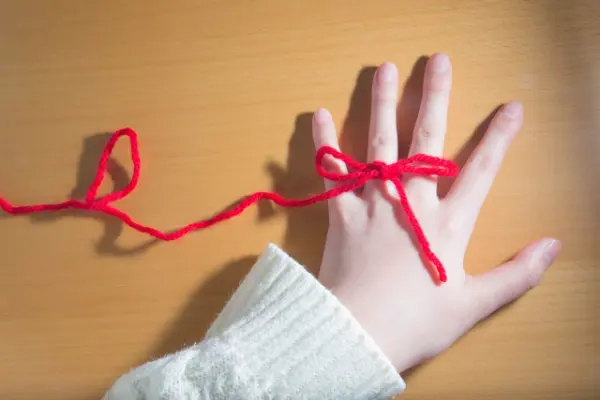 左手の薬指に巻かれた赤い毛糸の写真