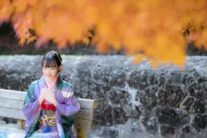 紅葉をバックにベンチに座る振袖姿の女性