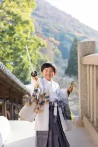 刀の小物を手にした男の子が回廊で誇らしげな笑顔を見せる七五三の記念写真