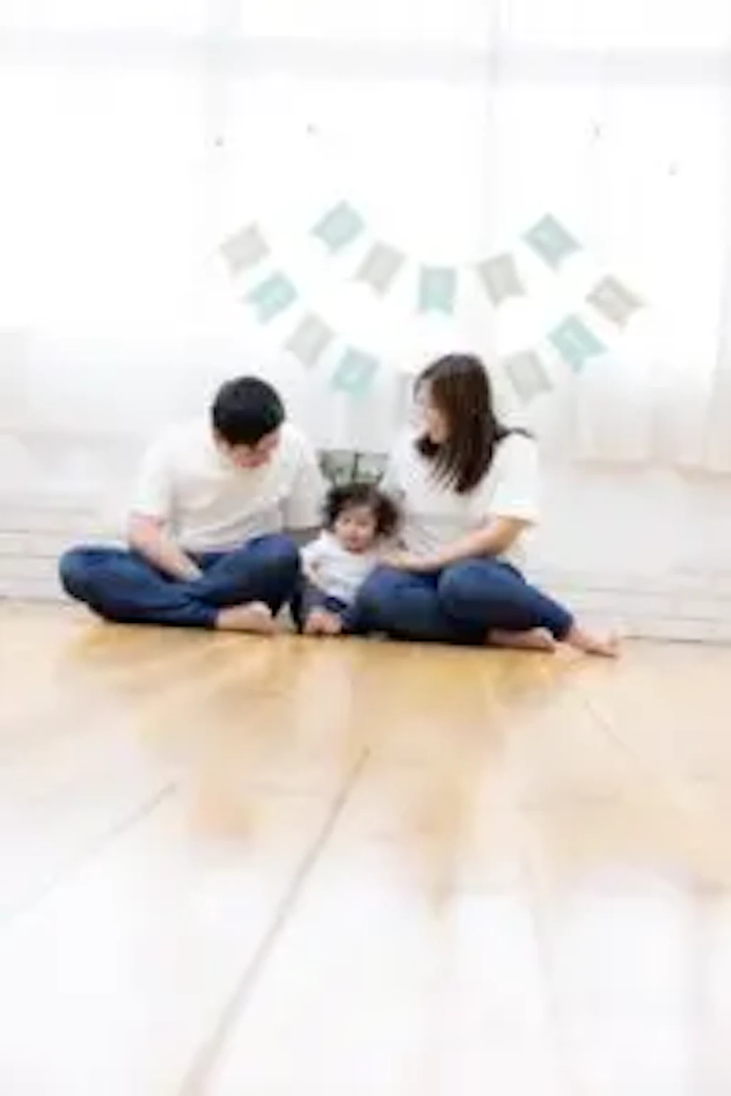 岡山のスタジオでお揃いの白い服を着て、床に座りながら寄り添う1歳の男の子とご両親