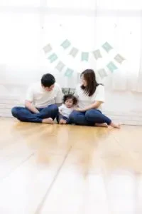 岡山のスタジオでお揃いの白い服を着て、床に座りながら寄り添う1歳の男の子とご両親
