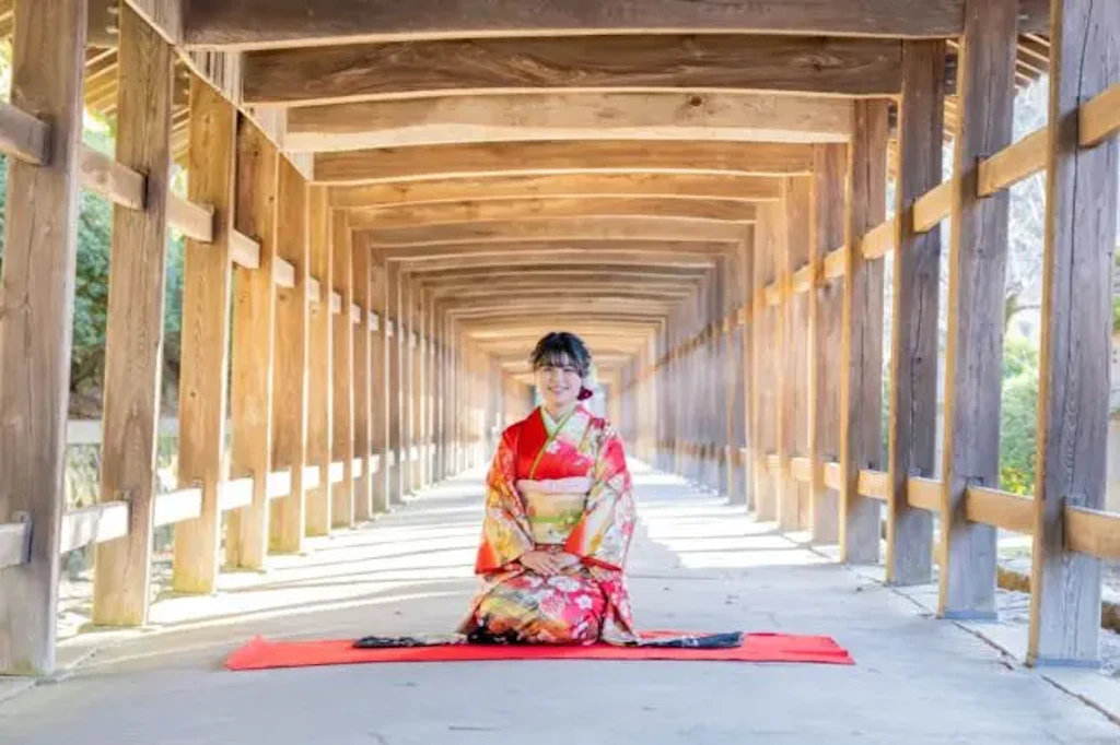 吉備津神社の回廊に正座して座る振袖姿の女性、奥まで一直線に続く木造建築が背景に広がる様子