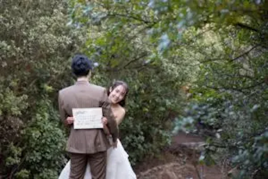 新郎新婦様が王子が岳の緑に囲まれた小道でメッセージボードを手に微笑む結婚式の前撮り