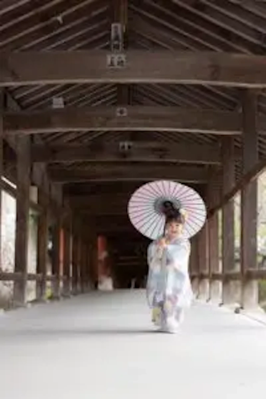 吉備津神社の回廊で和傘を差しながら歩く3歳の女の子の後ろ姿