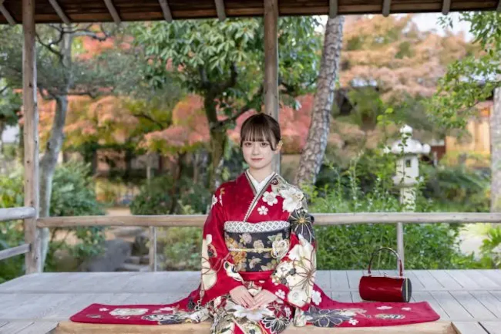紅葉を背景に縁側で赤い振袖姿の女性が正座している成人式の前撮り写真