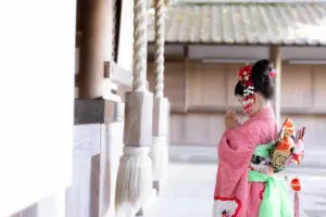 吉備津神社の本殿前で、後ろ姿の女の子が両手を合わせて静かに祈る七五三の一コマ