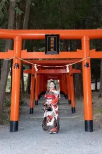 吉備津彦神社の朱色の鳥居が連なる参道で赤い振袖姿の女性が正面を向いて立っている